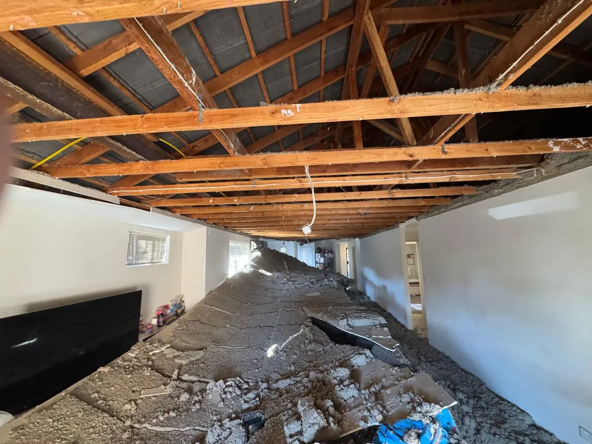 Collapsed plasterboard ceiling in an Ellenbrook lounge room, with insulation heaped across the floor and the roof battens exposed above