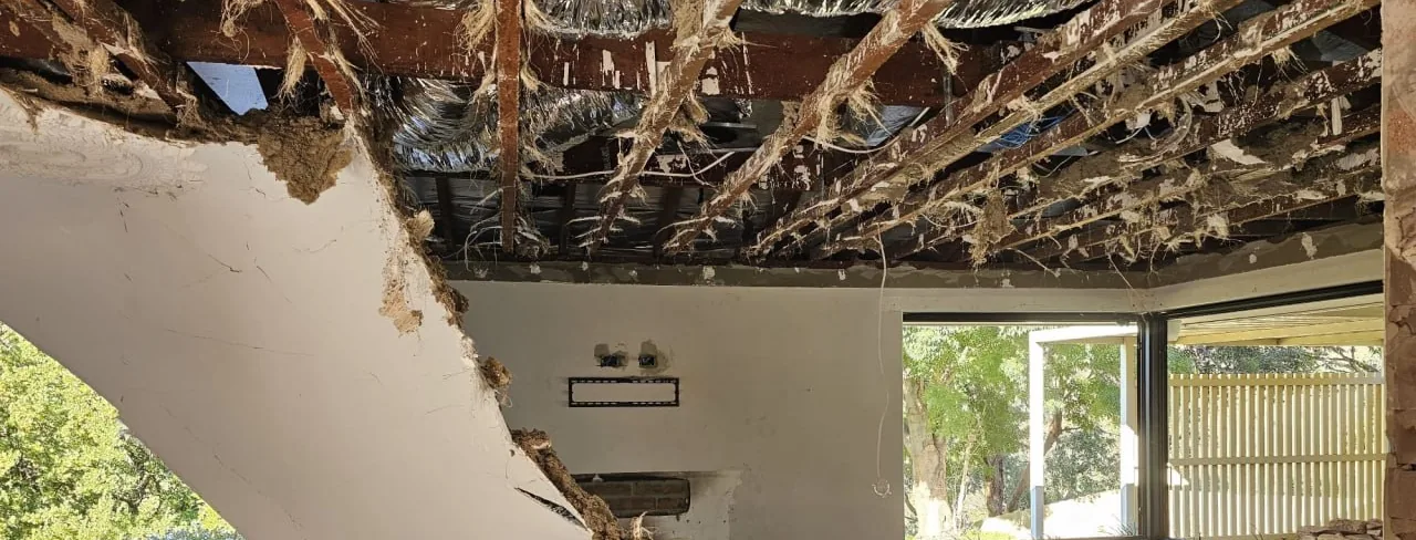 A large sheet of old plasterboard ceiling hanging down into a stripped room on Croydon Road, Roleystone, with the roof timbers exposed above it and the brick walls back to bare